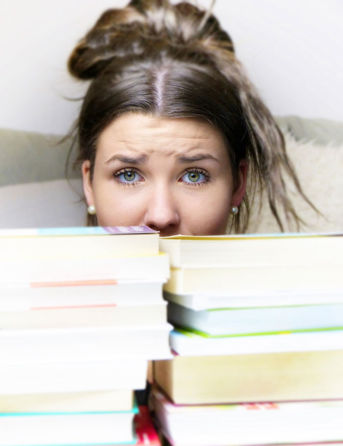 Teenage Girl Peeking Over Stack of Books